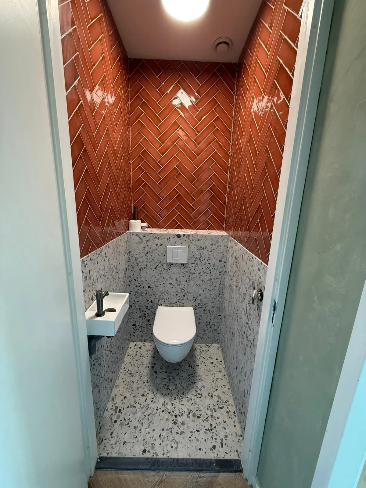 Toilet met terracottakleurige visgraattegels, terrazzo-look wand en hangtoilet