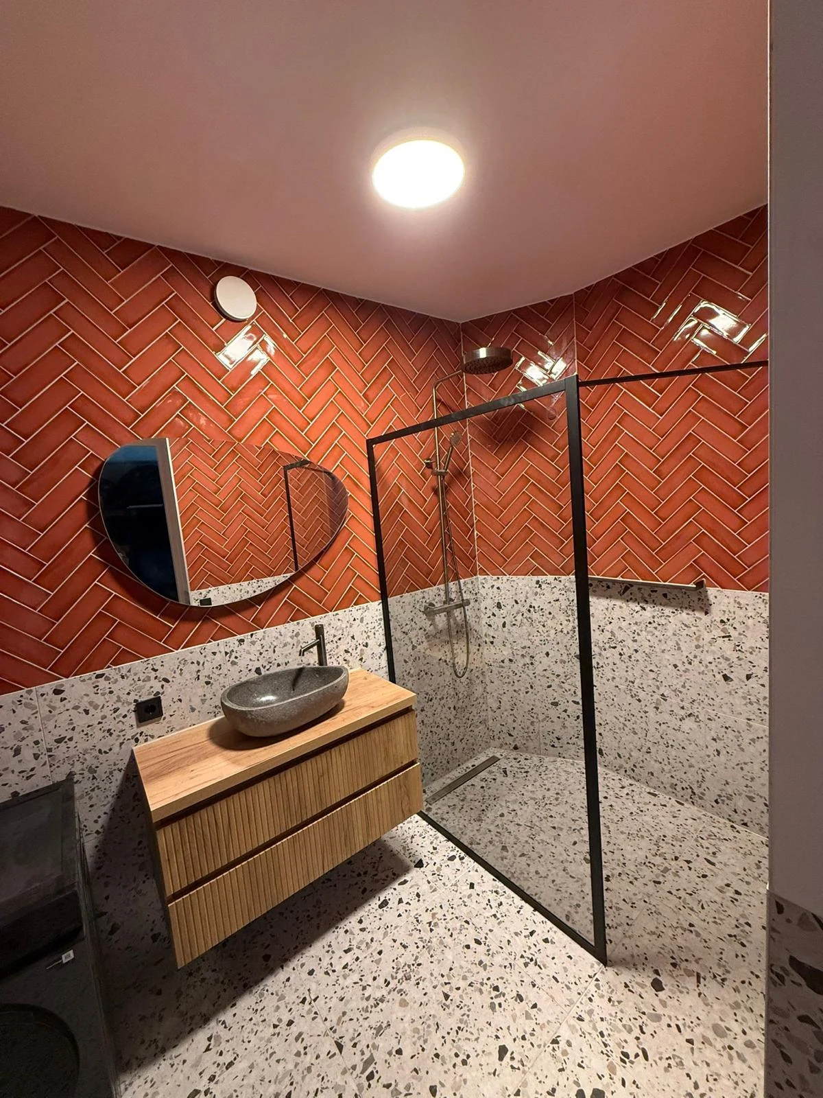 Overzicht met terracottakleurige visgraatwand, wastafel en glazen douchewand