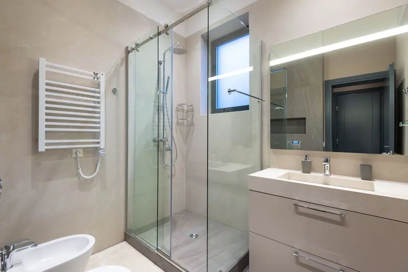 Badkamer met glazen douchecabine, handdoekradiator en wastafelmeubel