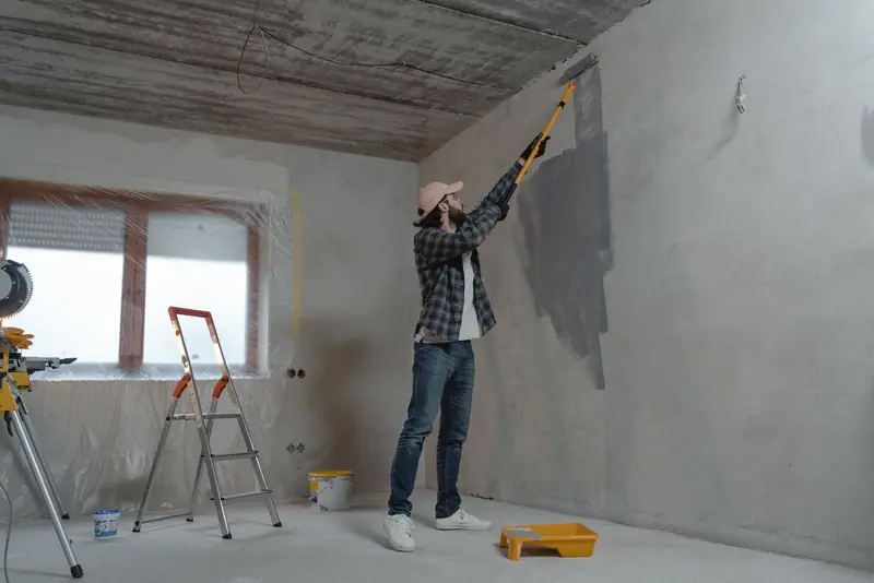 Schilder zet met een roller een grondlaag op een kale wand