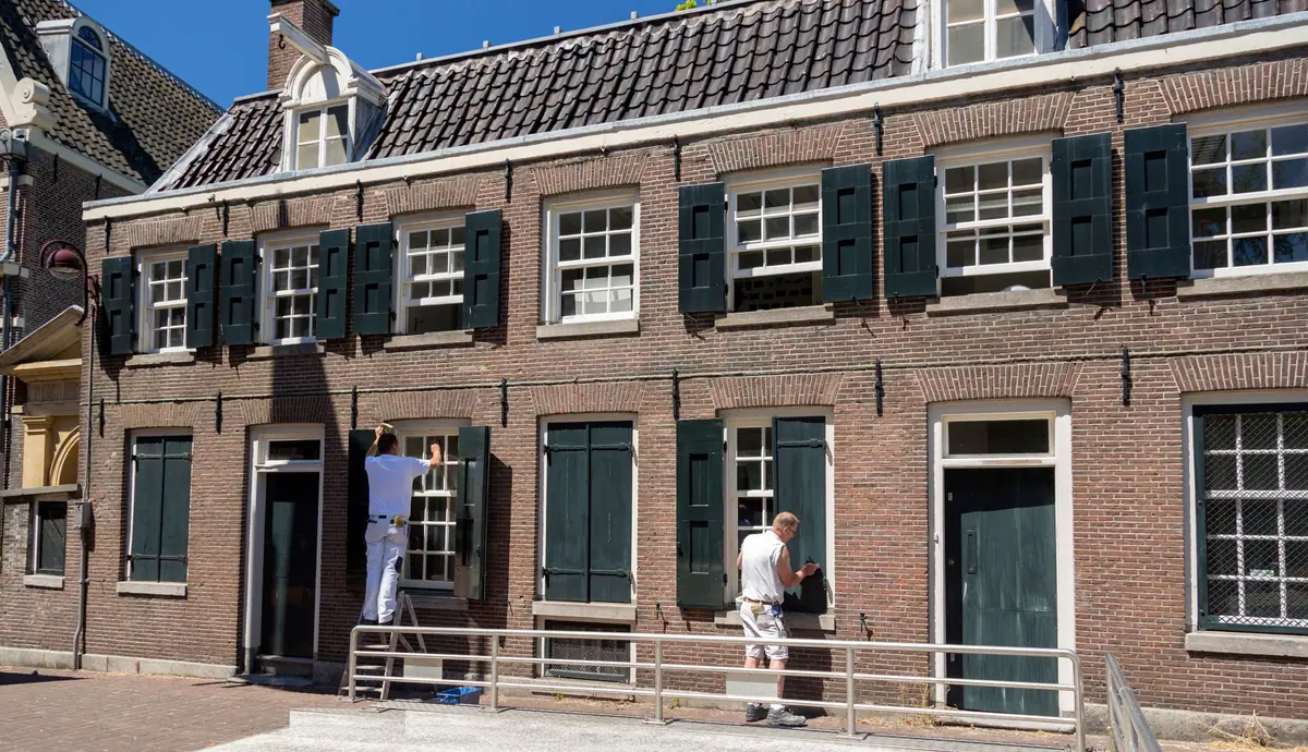Twee schilders werken aan de luiken en kozijnen van een bakstenen gevel